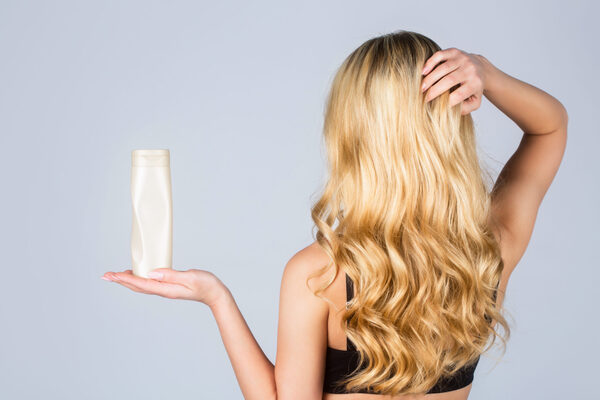 Woman with blonde hair, holding a bottle of organic shampoo made of hydrolysed proteins